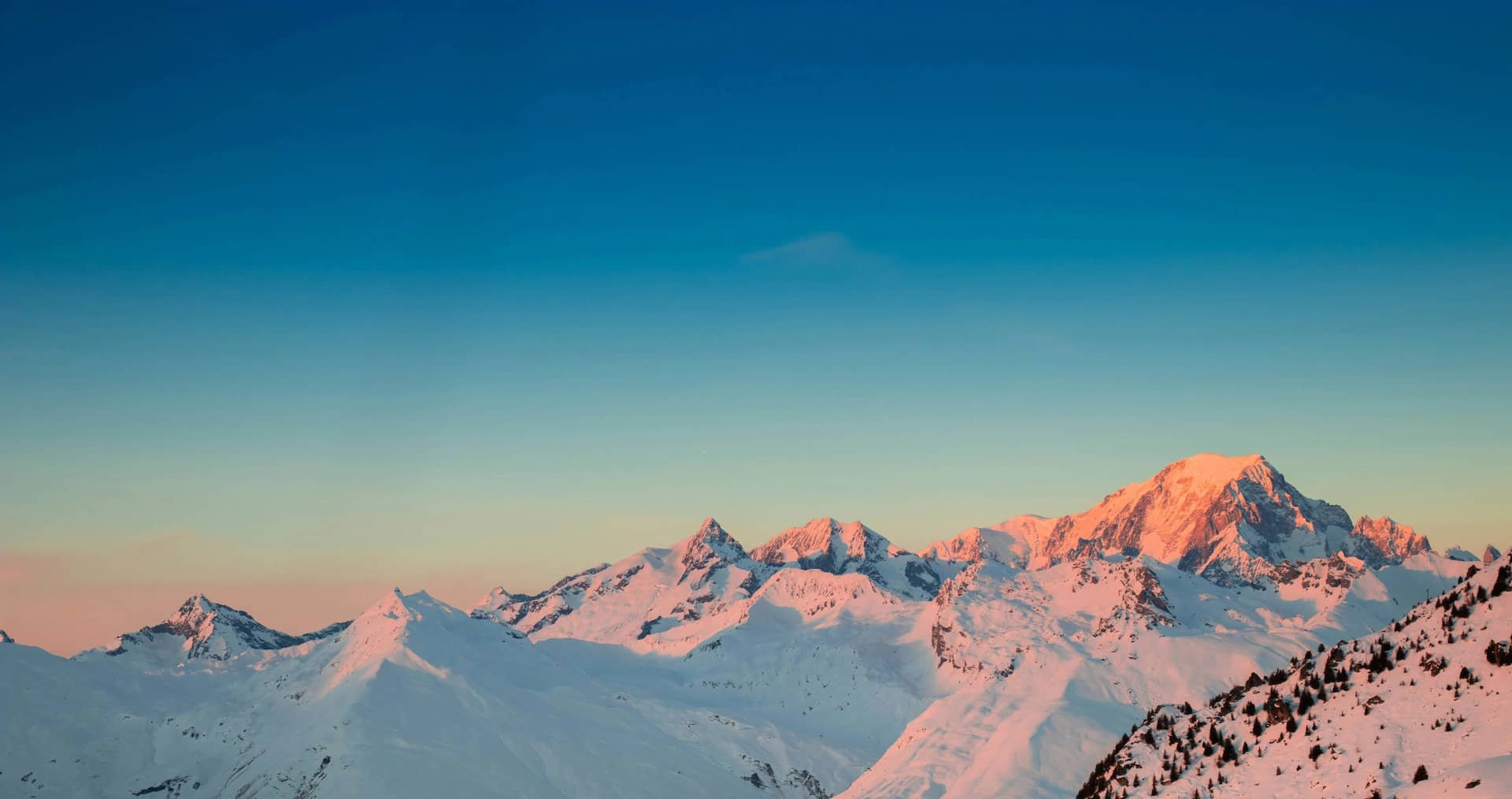Snowy mountain peaks glowing pink at sunset