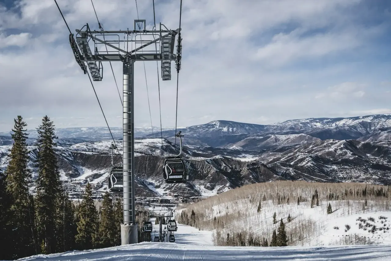 Gondola cabins climbing above a snowy, forested valley