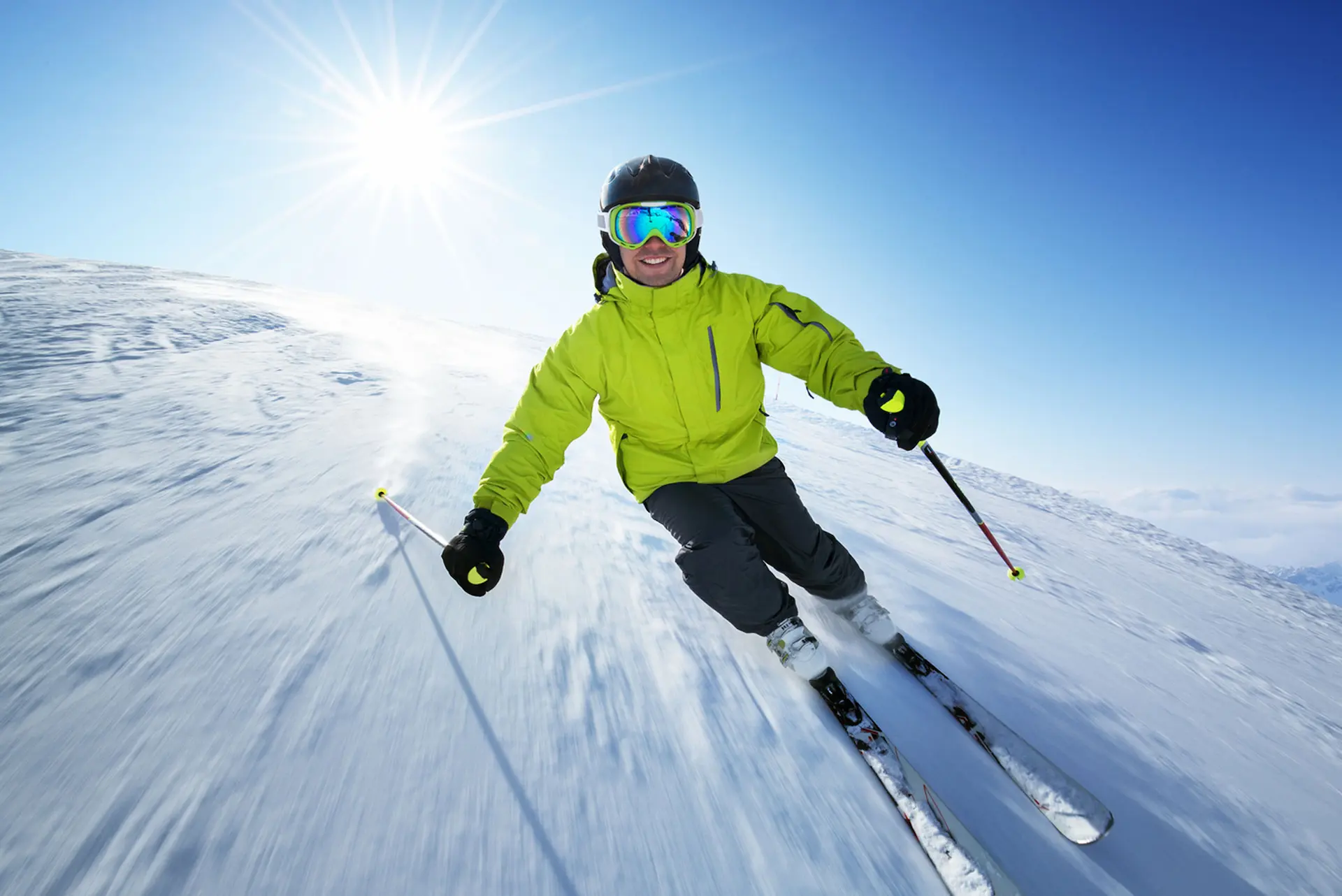 Skier in a green jacket carving down a groomed run on a sunny day